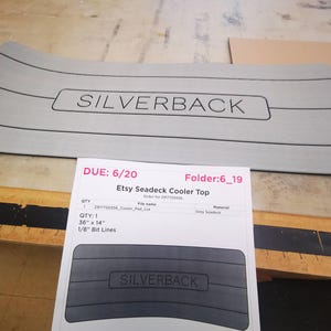 May include: A gray seadeck cooler top with the text "SILVERBACK" printed on it. The cooler top is 36 inches by 14 inches and has 1/8 inch bit lines.
