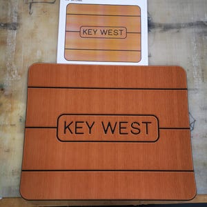 May include: A brown wooden cooler top with the text "KEY WEST" in black lettering. The top is 14.43 inches by 11.71 inches and has 1/8 inch bit lines.