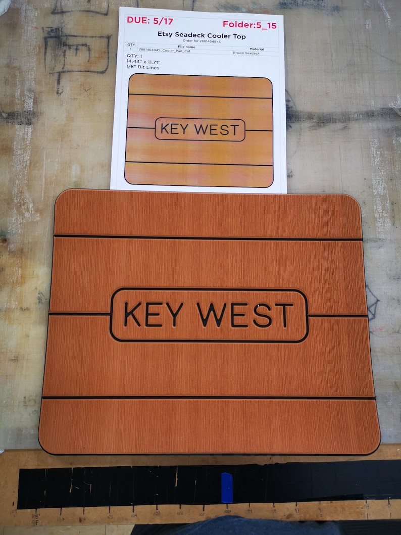 May include: A brown wooden cooler top with the text "KEY WEST" in black lettering. The top is 14.43 inches by 11.71 inches and has 1/8 inch bit lines.