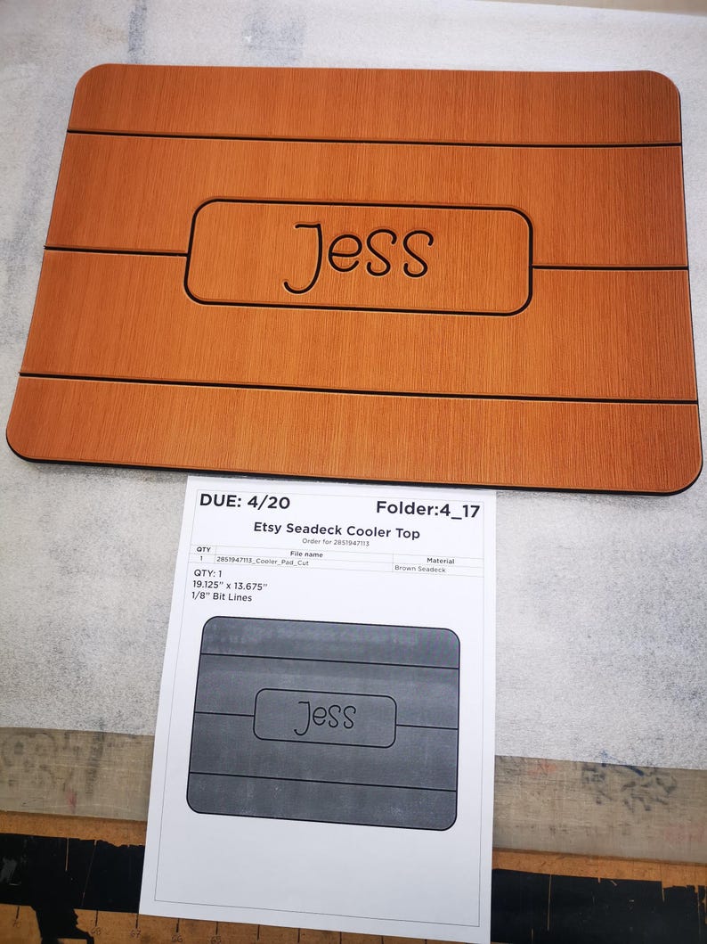 May include: A brown wooden cooler top with the name "Jess" engraved in the center. The top is 19.125 inches by 13.675 inches and has 1/8 inch bit lines.