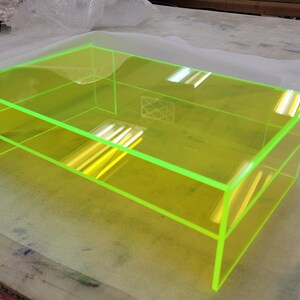 May include: A bright yellow coffee table with a clear acrylic top and a shelf. The table has a neon green edge.
