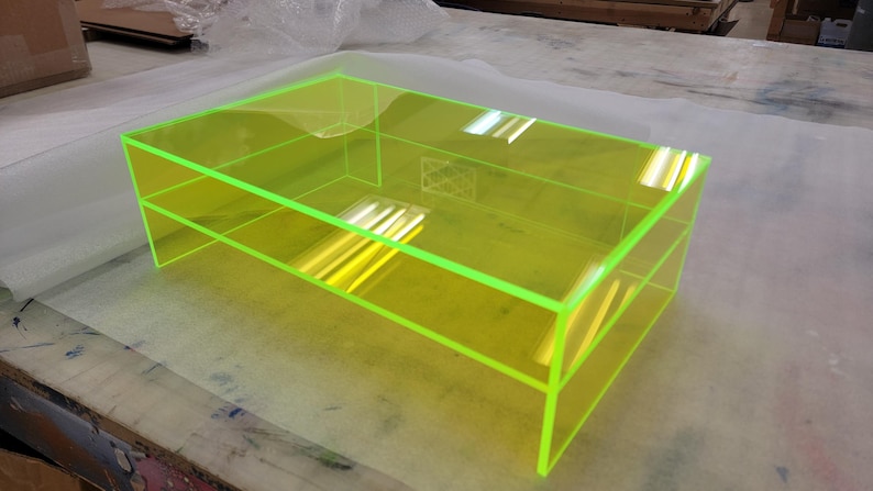May include: A bright yellow coffee table with a clear acrylic top and a shelf. The table has a neon green edge.