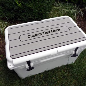 May include: White cooler with a gray, wood-look lid. The lid has a rectangular cutout with the text "Custom Text Here" in black.