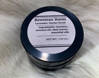 May include: A round, black container of beeswax balm with a white label. The label reads "Beeswax Balm Lavender Thyme Scent" and lists ingredients. The net weight is 28 grams.