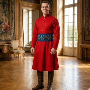 May include: A red tunic with a mandarin collar and long sleeves, accented by a blue and gold embroidered belt. The outfit is paired with brown leather boots. The person is standing in a room with large windows and ornate decor.