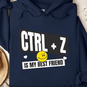 Może przedstawiać: Granatowa bluza z kapturem z białym nadrukiem "CTRL + Z is my best friend" i żółtą buźką.
