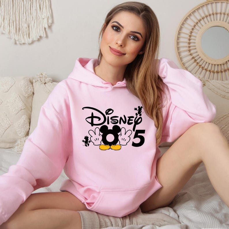 Op de afbeelding: Roze hoodie met een zwarte en gele Mickey Mouse-afbeelding en de tekst "Disney 5".