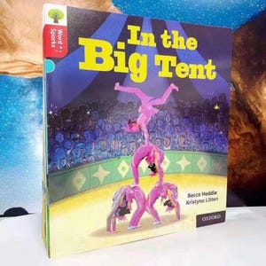 Può includere: Un libro per bambini intitolato In the Big Tent con un'illustrazione di copertina di tre acrobati in body rosa che eseguono una piramide in un circo. Lo sfondo mostra un vasto pubblico in un tendone illuminato di blu. Autori: Becca Heddle e Kristyna Litten.