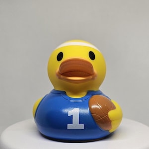 May include: A yellow rubber duck wearing a blue jersey with the number "1" and holding a brown basketball.