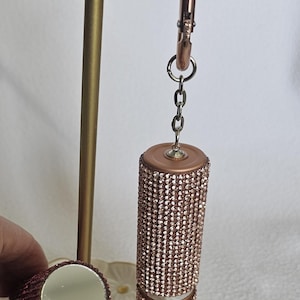 Puede incluir: Un estuche de l&aacute;piz labial de oro rosa incrustado con peque&ntilde;os pedrer&iacute;a brillantes. El estuche de l&aacute;piz labial est&aacute; sujeto a una cadena y un clip de oro rosa. Tambi&eacute;n se ve un peque&ntilde;o espejo redondo de oro rosa.