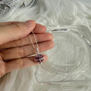 Op de afbeelding: Een zilveren ketting met een hanger van paarse amethist. De hanger is een bol met een zilveren band in het midden.