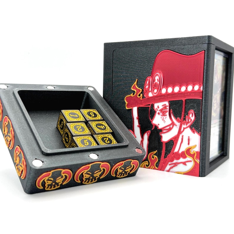 May include: Black and red card game storage box and dice tray. The box features a red and black graphic of a character with a hat. The dice tray contains six gold and black dice. The tray and box have a skull design.