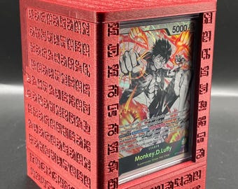 May include: A red, 3D printed card display case with a black and white anime card featuring a character with black hair and a red background. The card has the text "Monkey.D.Luffy" and "Supernova: Straw Hat Crew".