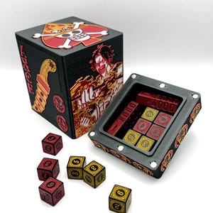 May include: Black box with red and gold accents, featuring a skull and crossbones design and the word "ACE". The box is open, revealing dice and a storage compartment. Several dice are scattered around the box, with red and gold coloring.