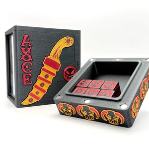 May include: A black dice box and tray set with red and yellow accents. The box features the word "AXCE" and a stylized knife design. The tray holds six red dice with white numbers and is decorated with skull motifs.
