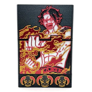 May include: Black rectangular case featuring a red, white, and gold illustration of a character with flames. The case has three skull designs at the bottom. The character is depicted with an open mouth and intense expression.