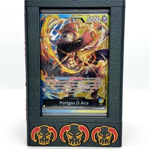 May include: A black card holder with a clear window displaying a trading card. The card features a character with a hat and flames, with text that reads "Portgas.D.Ace". The holder has three skull and flame designs.