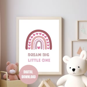 May include: A framed print with a pink and maroon rainbow design and heart details. The text "DREAM BIG LITTLE ONE" is below the rainbow. A digital download sticker is in the lower left corner. The print is displayed in a nursery setting.