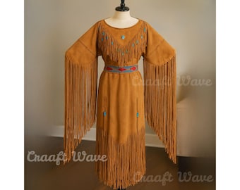 May include: A tan suede dress featuring long, flowing fringe on the sleeves and hem. The garment includes a decorative beaded belt with red and blue patterns, and small turquoise-colored accents on the chest and skirt area, displayed on a mannequin.