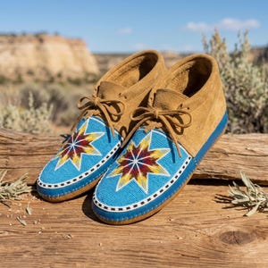 May include: A pair of tan suede moccasins featuring blue beaded vamps with a multi-colored star pattern in red, yellow, and white. The shoes have matching tan suede laces, a blue leather trim, and a white and black beaded border along the edge.