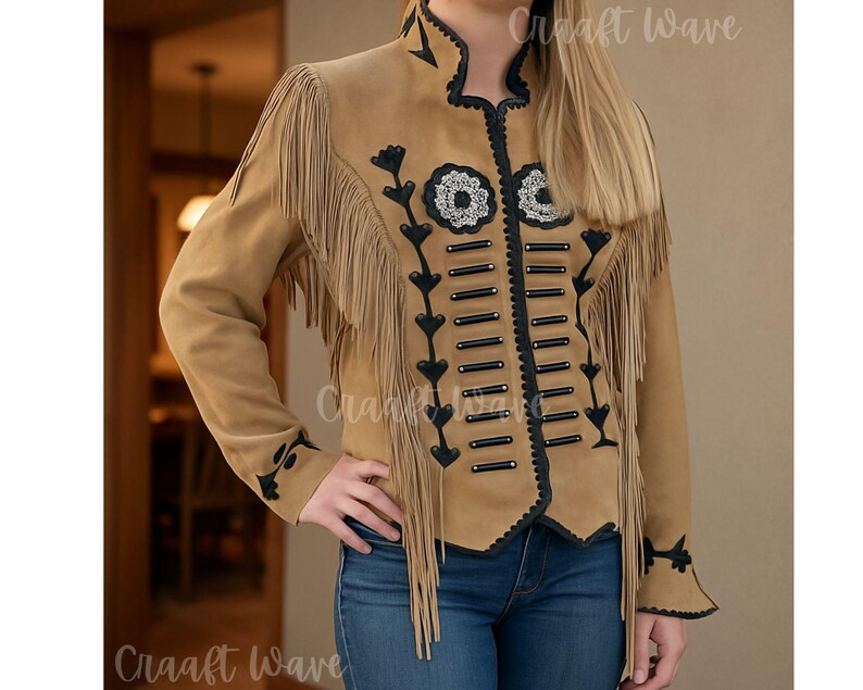May include: A tan jacket featuring long fringe detailing on the shoulders and chest. The garment includes black trim, decorative black horizontal bars, and floral embroidery on the front. The jacket has long sleeves and a high collar design.