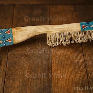 May include: A tan leather sheath with beaded turquoise, red, and white geometric designs on each end. The sheath has a fringe along the bottom edge. The item is displayed on a dark wood surface.