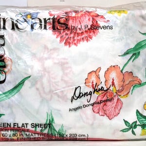 Könnte beinhalten: Ein Queen-Size-Flachbettlaken in einer Plastikverpackung. Das Laken hat ein Blumenmuster mit rosa, orangefarbenen und gelben Blumen sowie grünen Blättern auf weißem Hintergrund. Der Text "fine arts" und "Utica" sind sichtbar.