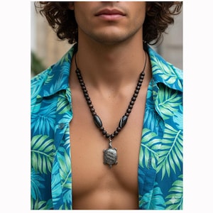 May include: A necklace with a silver turtle pendant and dark brown wooden beads. The pendant is a silver turtle. The person in the image is wearing a blue and green tropical print shirt.