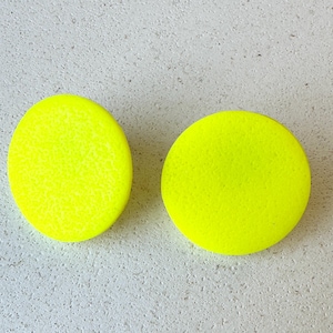 May include: A pair of bright yellow round earrings. The earrings are made of a smooth, textured material.