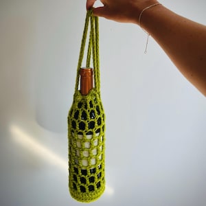 Pode incluir: Um porta-garrafas de vinho de crochê verde com uma garrafa de vinho dentro.