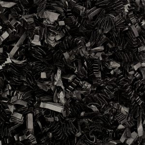 May include: A full-frame shot of a pile of black shredded paper. The paper is cut into various shapes and sizes, creating a textured, layered appearance. The lighting is even, highlighting the different folds and edges of the paper.