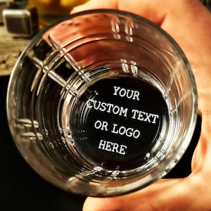 Könnte beinhalten: Ein klares Glas Whiskeyglas mit dickem Boden und einem strukturierten Design. Das Glas hat einen geätzten Kreis im Boden mit dem Text "YOUR CUSTOM TEXT OR LOGO HERE".