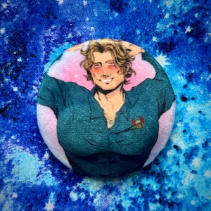 Pode incluir: Um botão redondo com uma ilustração de uma pessoa com cabelo loiro e uma camisa verde-azulado. A pessoa está sorrindo com os braços atrás da cabeça. O fundo é rosa com pequenas estrelas rosas.