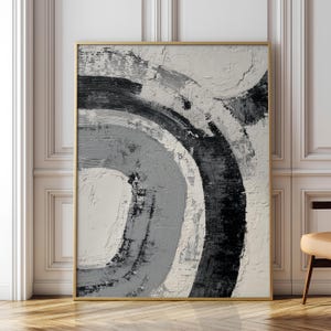 Peut inclure: Tableau abstrait encadré d'or, avec un design texturé et superposé. L'œuvre présente des coups de pinceau incurvés en nuances de gris, noir et blanc, créant une esthétique moderne et minimaliste. Le tableau est accroché sur un mur blanc.
