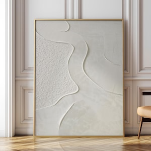 Puede incluir: Una obra de arte abstracta enmarcada. La obra presenta un diseño texturizado en blanco roto con formas orgánicas fluidas. El marco es de color dorado fino. El arte se exhibe contra una pared blanca.