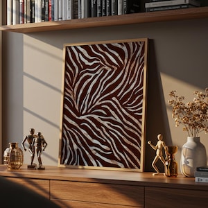 Peut inclure: Une œuvre d'art murale encadrée rectangulaire présentant un motif de rayures de zèbre à fort contraste en argent métallique sur un fond brun foncé profond. L'impression est insérée dans un cadre en bois clair et posée sur une surface en bois.