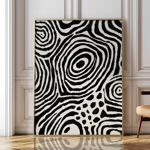 Peut inclure: Une œuvre d'art murale rectangulaire présentant un motif abstrait à fort contraste noir et blanc cassé, composé de lignes circulaires concentriques et de formes organiques. L'œuvre est encadrée d'un fin cadre doré à la finition texturée.