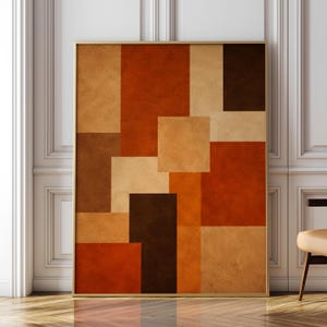 Könnte beinhalten: Ein rechteckiger Wandkunstdruck mit einer geometrischen Komposition aus überlappenden Quadraten und Rechtecken in verschiedenen Schattierungen von gebranntem Orange, Terrakotta, Hellbraun und Dunkelbraun, eingefasst in einen dünnen, goldfarbenen Metallrahmen.