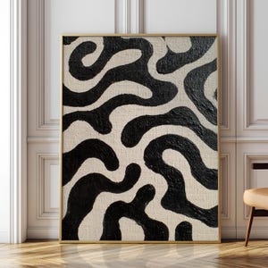 Peut inclure: Impression d'art abstrait avec un motif noir et blanc. L'œuvre d'art présente un fond beige avec des formes organiques épaisses, noires et fluides. L'œuvre est encadrée dans un cadre doré et est exposée contre un mur blanc.