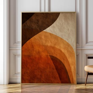 Puede incluir: Una impresión artística abstracta enmarcada con formas curvas en capas en tonos de marrón, naranja y beige. La obra de arte tiene una apariencia texturizada y se muestra en un marco dorado. La pieza está contra una pared blanca.