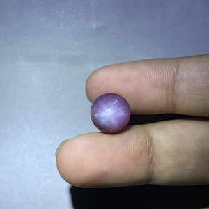 May include: A round, purple star ruby gemstone with a six-pointed star in the center.