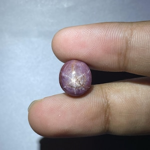 Könnte beinhalten: Ein runder, rosafarbener Sternrubin-Edelstein mit einem sechszackigen Stern in der Mitte.