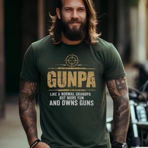 Può includere: Una maglietta verde con una grafica dorata che dice "Gunpa Like a normal grandpa but more fun and owns guns". La grafica include anche un simbolo di bersaglio.