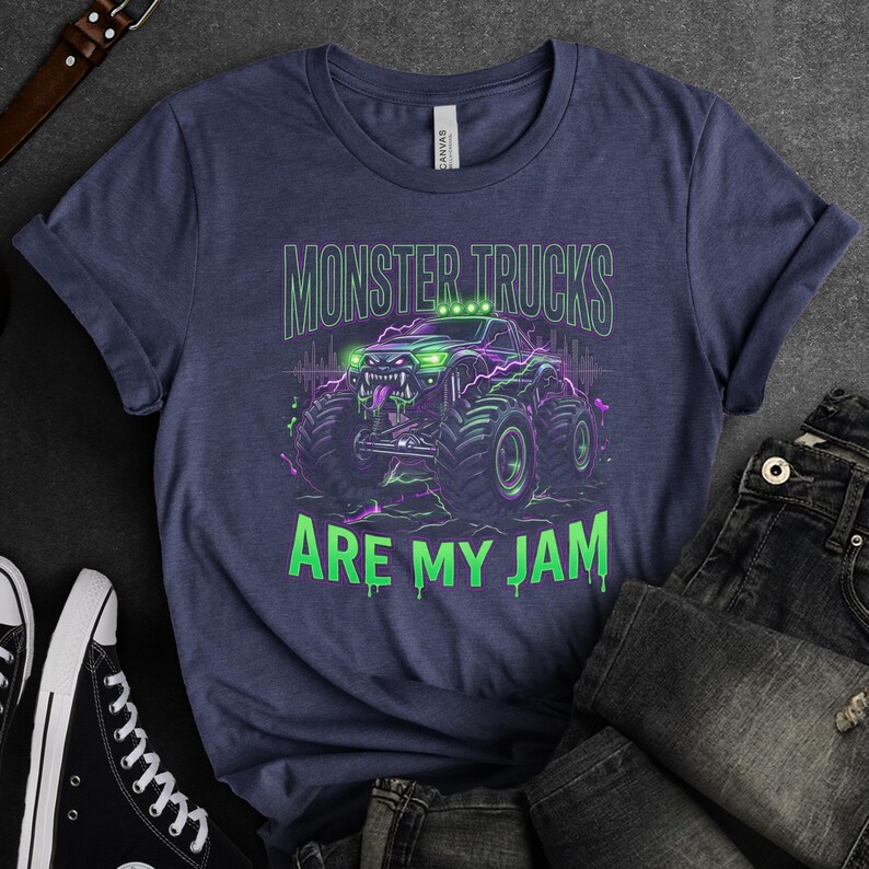 Pu&ograve; includere: T-shirt blu navy con grafica di monster truck e la scritta "MONSTER TRUCKS ARE MY JAM" in verde e viola. Il design presenta un monster truck con ruote grandi e un'espressione minacciosa.