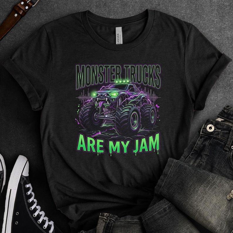 Pu&ograve; includere: T-shirt nera con grafica di monster truck verde e viola, con la scritta "MONSTER TRUCKS ARE MY JAM". Il monster truck ha pneumatici grandi e un design minaccioso.