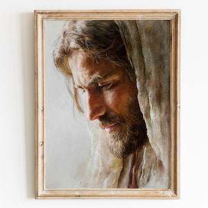 May include: A framed portrait of a man with long, light brown hair and a beard, looking down. The artwork is in a wooden frame and is set against a white background. The man is wearing a white cloth draped over his head and shoulders.