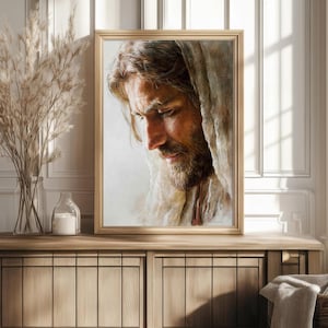 May include: Framed portrait of a man with long hair and a beard, gazing downward. The artwork is in a gold frame and is displayed on a wooden cabinet. The portrait is a close-up, showing the man's face and shoulders.