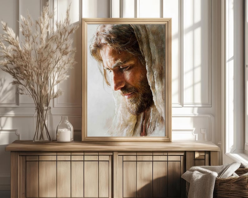 May include: Framed portrait of a man with long hair and a beard, gazing downward. The artwork is in a gold frame and is displayed on a wooden cabinet. The portrait is a close-up, showing the man's face and shoulders.