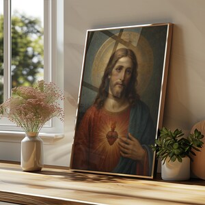 May include: A framed vertical wall art print depicting a portrait of a figure with long brown hair and a beard, wearing a red tunic and blue cloak, featuring a glowing heart emblem on the chest and a circular golden halo against a dark background.
