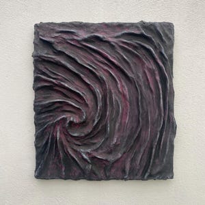 May include: A square, textured wall art piece with a swirling pattern in shades of dark grey and purple.
